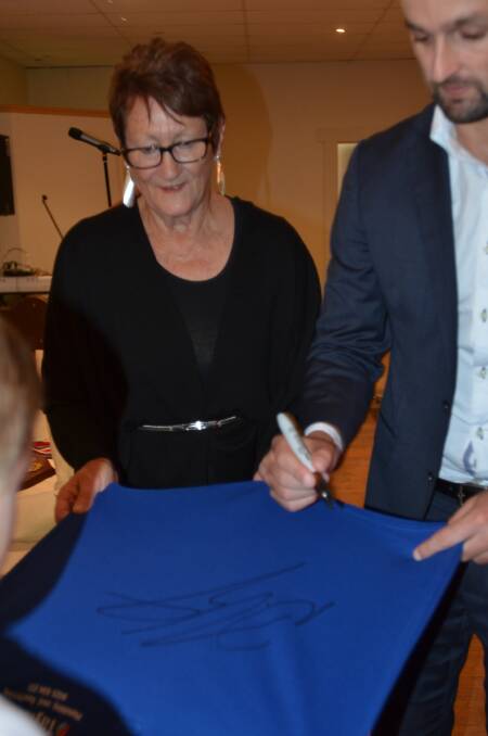 Kerre Mayo helping Nathan sign her grandchildren's cricket shirts.