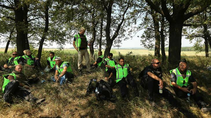 Dutch and Malaysian police take shelter from the sun as they await news on the outskirts of Rassypnoye near the crash site. Photo: Kate Geraghty