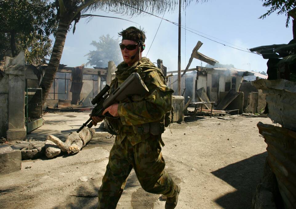 An Australian peacekeeper runs past a smouldering house on June 4, 2006 in Dili, East Timor. Photo by Paula Bronstein/Getty Images