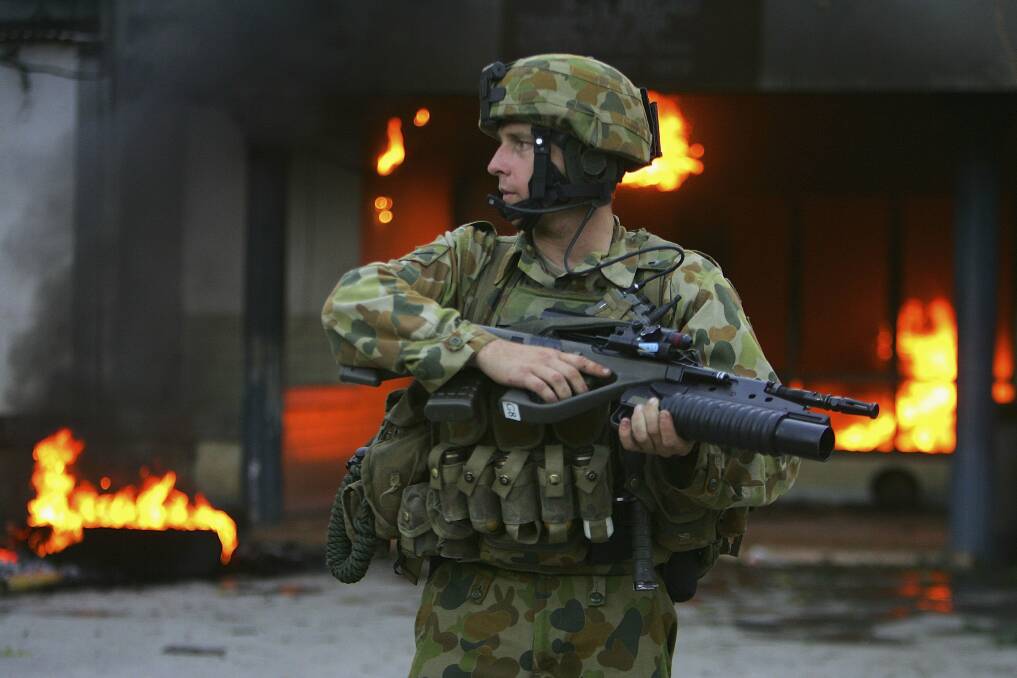 An Australian peacekeeping soldier stands guard next to a burning house on June 5, 2006 in Dili, East Timor. Photo by Paula Bronstein /Getty Images