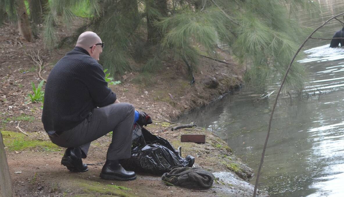 SEARCH: A Young Police detective examines a bag of clothing pulled out of the creek. 